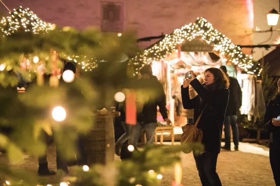 Woman taking photo at festive Christmas market with lights and decorated stalls