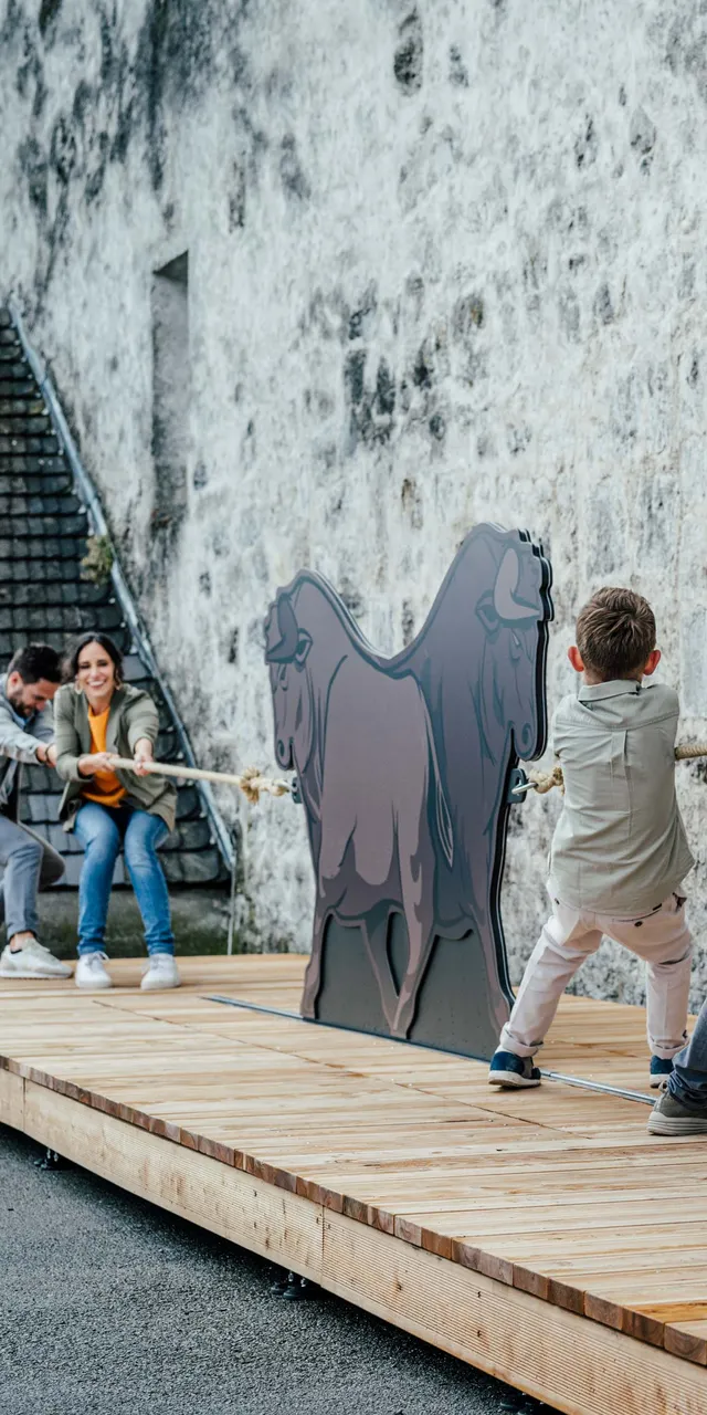 Bambini e adulti giocano al tiro alla fune con sagoma di toro su piattaforma in legno