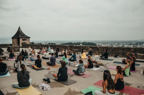 Lezione di yoga all’aperto con molte persone che meditano su tappetini con vista sulla città