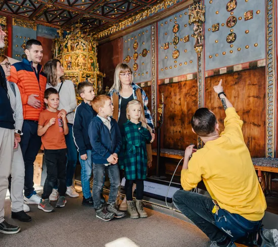 Reiseleiter zeigt einer Gruppe von Kindern und Erwachsenen historische Verzierungen im Museumsraum