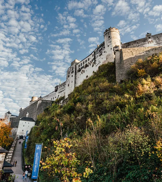 Fortezza Hohensalzburg su una collina con foglie autunnali e cielo azzurro con nuvole