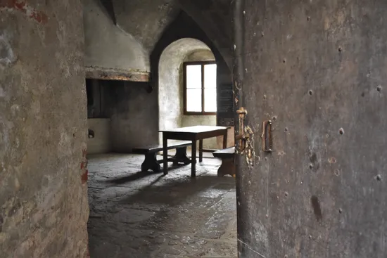 Mittelalterlicher Steinraum mit Holztisch und Bänken neben gewölbtem Fenster