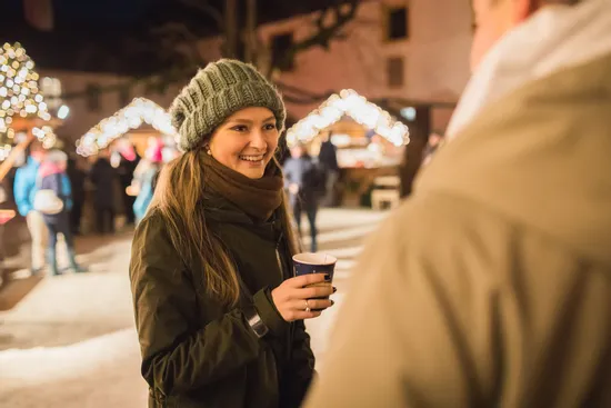 Smiling woman with hot drink at Christmas market in winter clothing