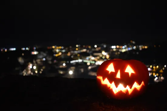 Zucca di Halloween illuminata con volto intagliato e luci della città sullo sfondo notturno