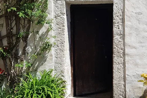 Rustic wooden door set in a stone frame surrounded by garden plants and flowers