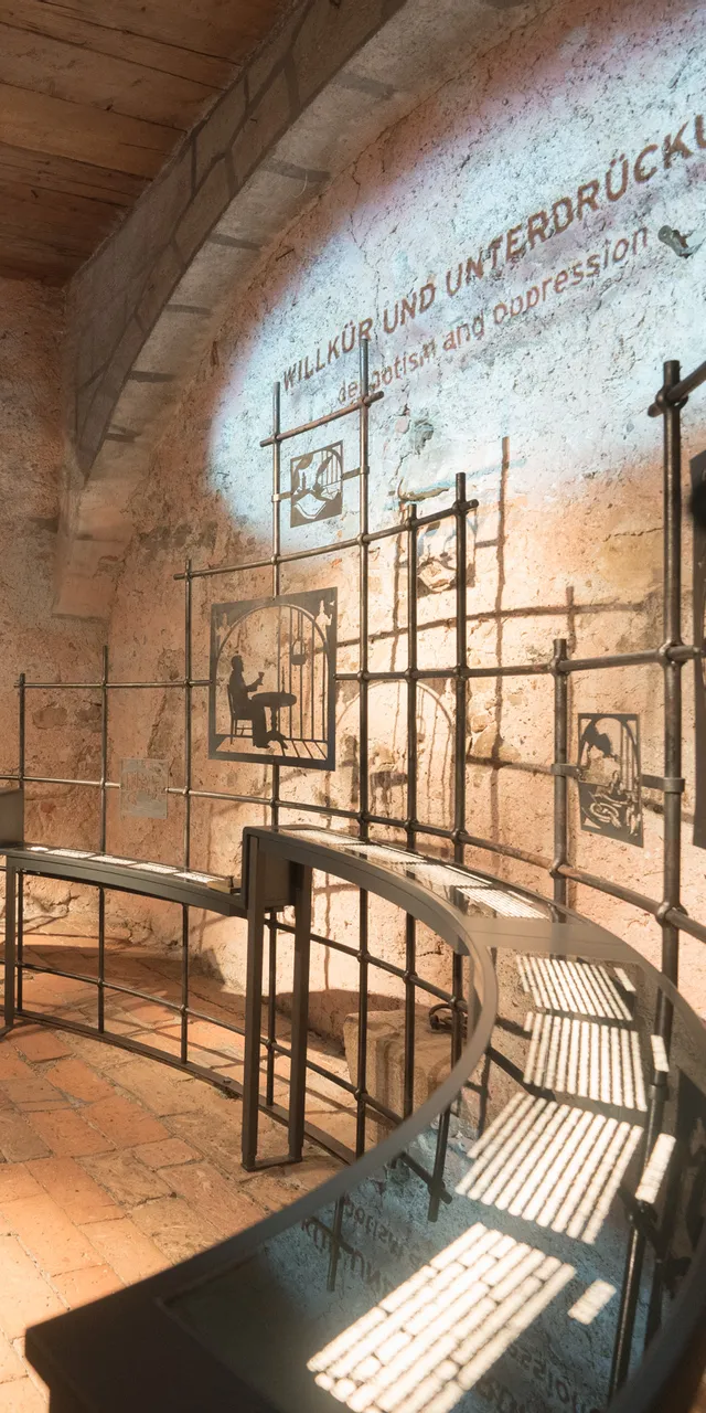 Historical museum exhibit on scapegoats and oppression in a stone-walled room with metal displays