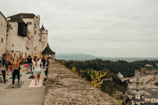 Sessione di yoga di gruppo sulla terrazza di un castello con vista su Salisburgo e paesaggio montano