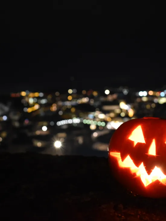 Leuchtender Halloween-Kürbis mit geschnitztem Gesicht vor nächtlicher Stadtkulisse