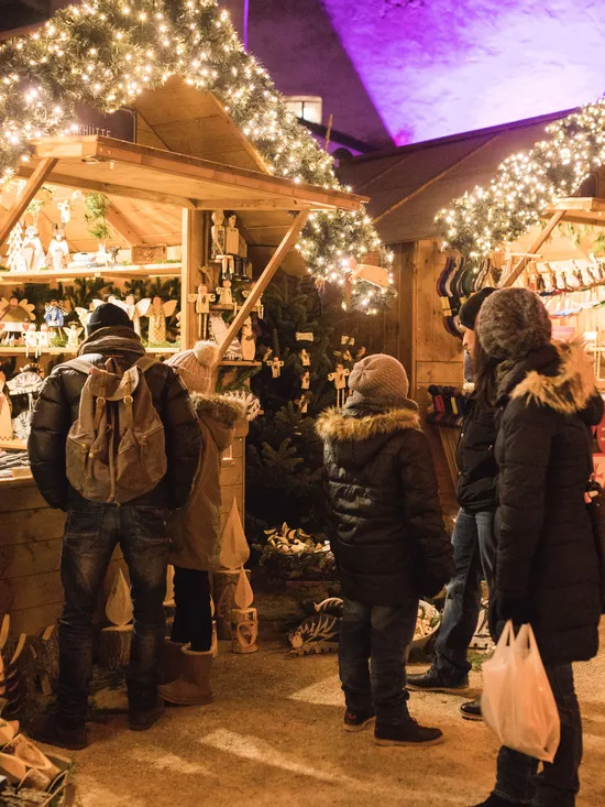 People shopping at wooden stalls decorated with Christmas lights at a festive market