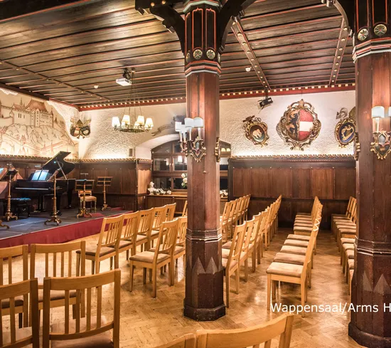 Sala da concerto con sedie in legno, pianoforte a coda, luci da palco e stemmi medievali