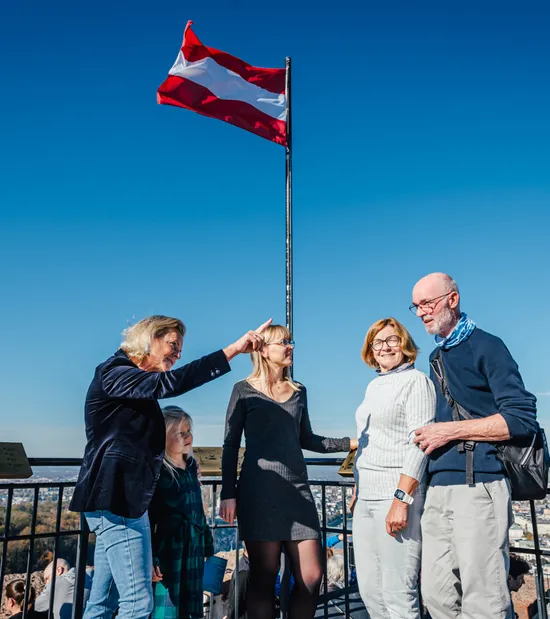 Group of people enjoying scenic city view under Austrian flag on sunny day