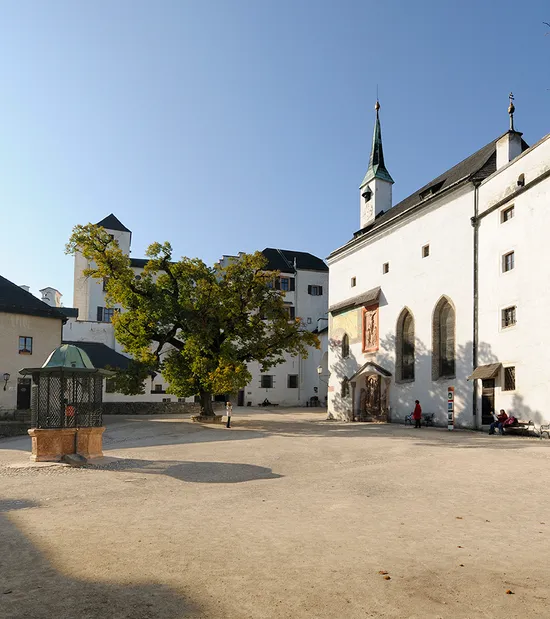Cortile interno della Fortezza Hohensalzburg con edifici storici e grande albero sotto cielo sereno