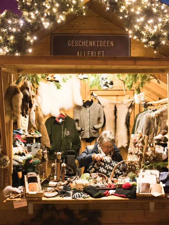 Weihnachtsmarktstand mit handgemachter Winterkleidung, Geschenken und warmer Beleuchtung