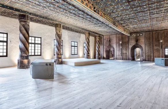 Historischer Saal mit verzierten Säulen, Holzboden und dekorierter Decke