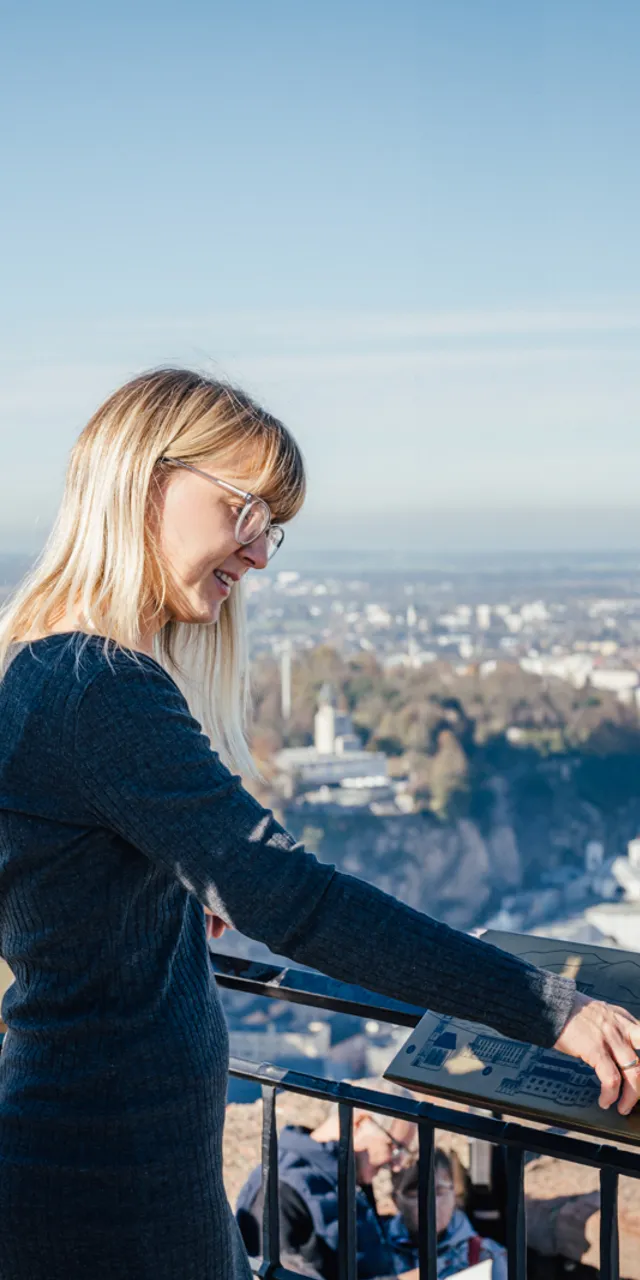Touristen lesen Infotafel mit Panoramablick über Salzburg