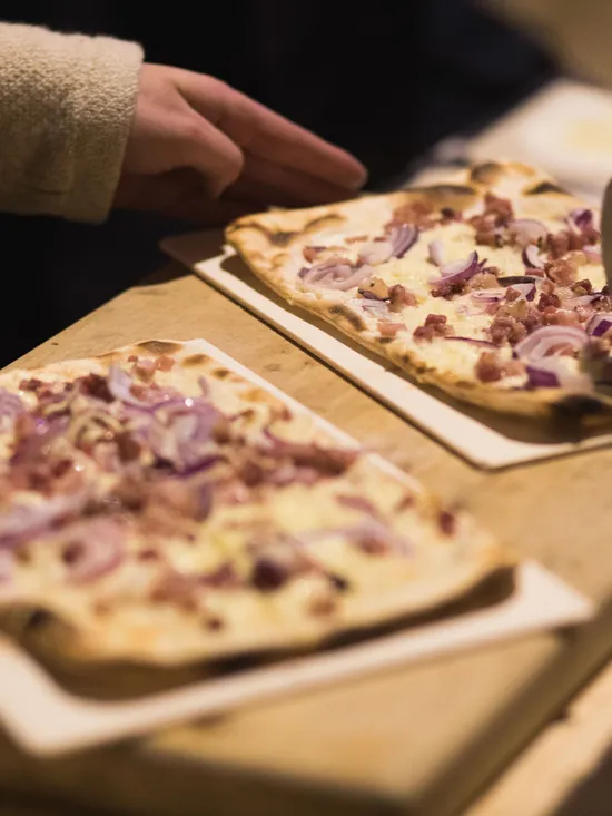 Freshly baked Flammkuchen with bacon and red onions being sliced on wooden counter