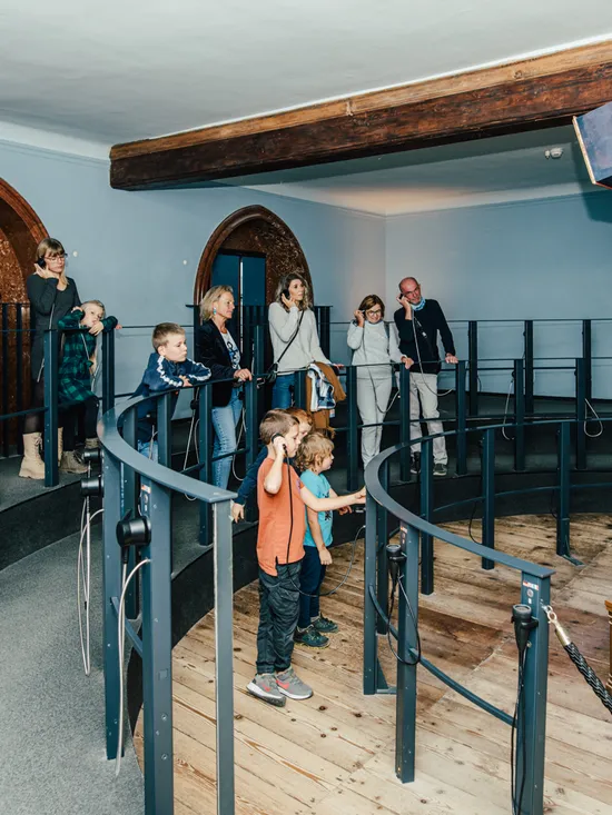 Visitors using audio guides to view a historical mechanical display in a museum