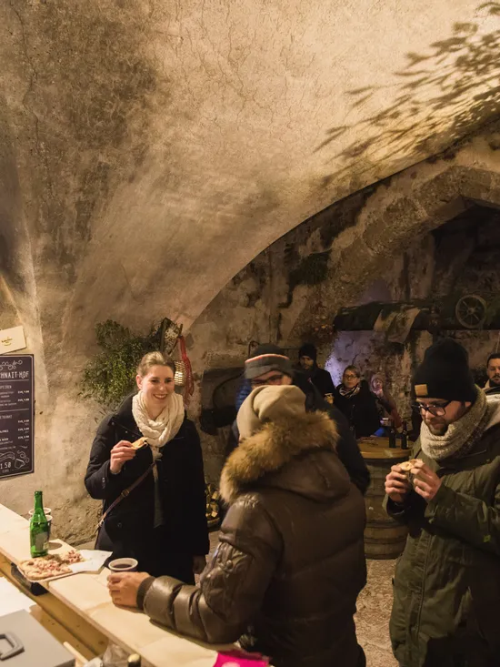 People enjoying food and drinks inside a rustic vaulted cellar with stone walls