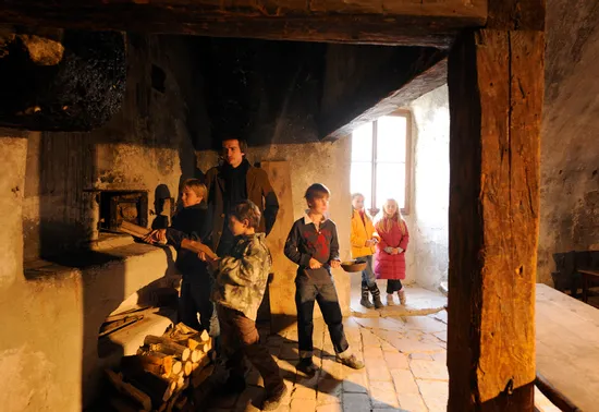 Children and adult in historical kitchen placing wood in old stone oven