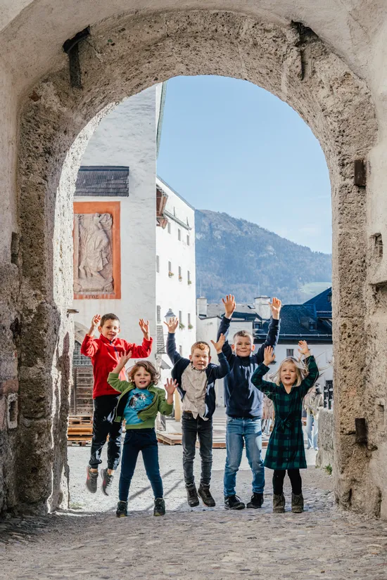 Fröhliche Kinder springen gemeinsam unter Steinbogen in historischer europäischer Stadt