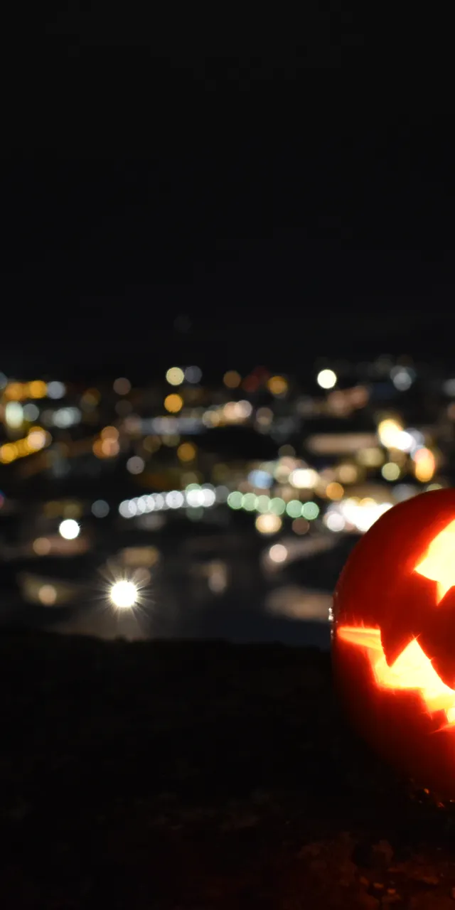 Leuchtender Halloween-Kürbis mit geschnitztem Gesicht vor nächtlicher Stadtkulisse