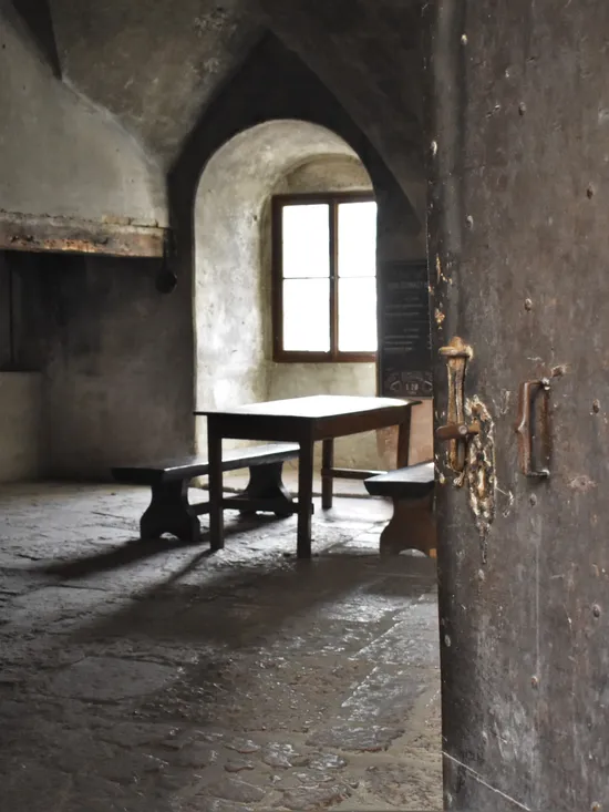 Mittelalterlicher Steinraum mit Holztisch und Bänken neben gewölbtem Fenster