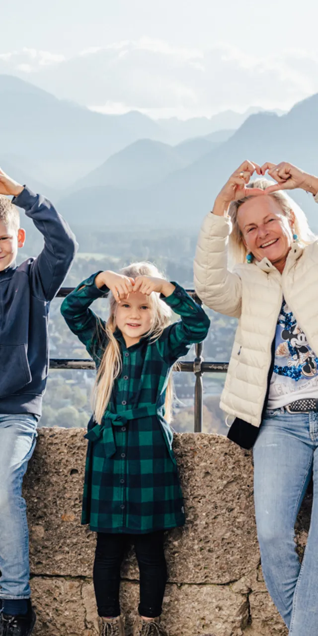 Smiling family making heart signs with hands against mountain and valley backdrop