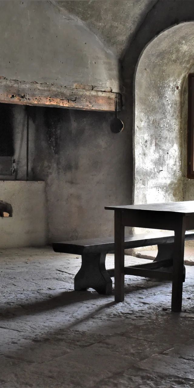 Rustic stone kitchen interior with wood-fired oven, long table and benches by arched window