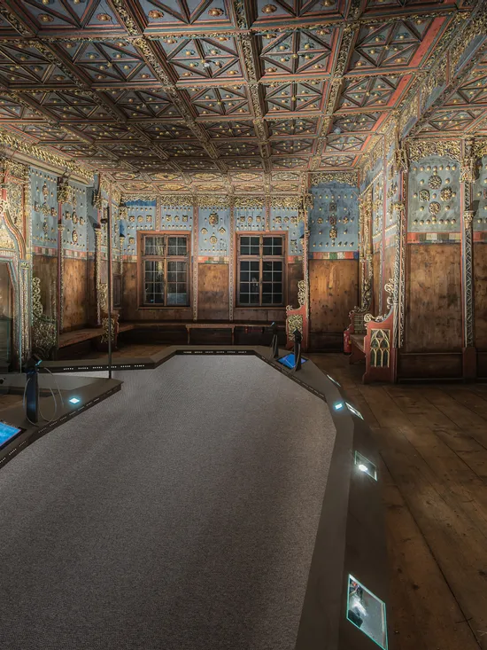 Prächtiger historischer Holzsaal mit bemalter Decke und geschnitzten Bänken in einer Museumsausstellung