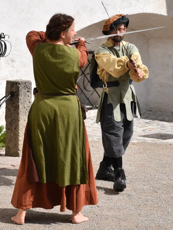 Two people in medieval costumes practicing sword fighting outdoors