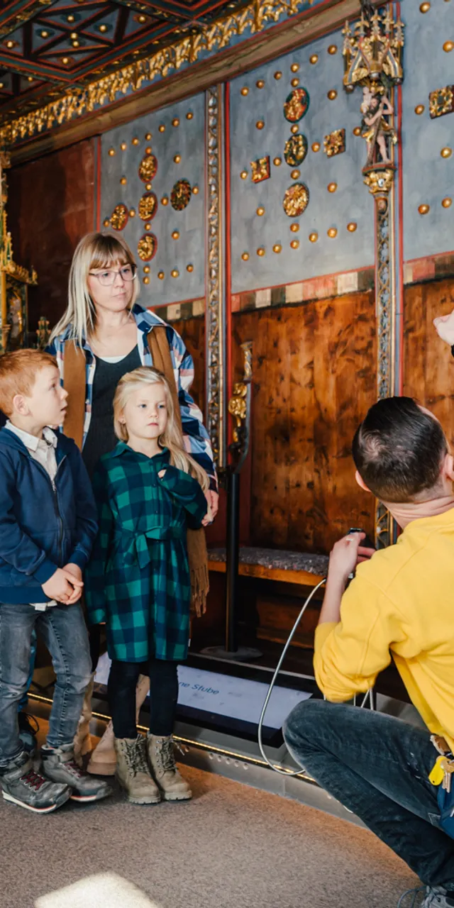 Reiseleiter zeigt einer Gruppe von Kindern und Erwachsenen historische Verzierungen im Museumsraum