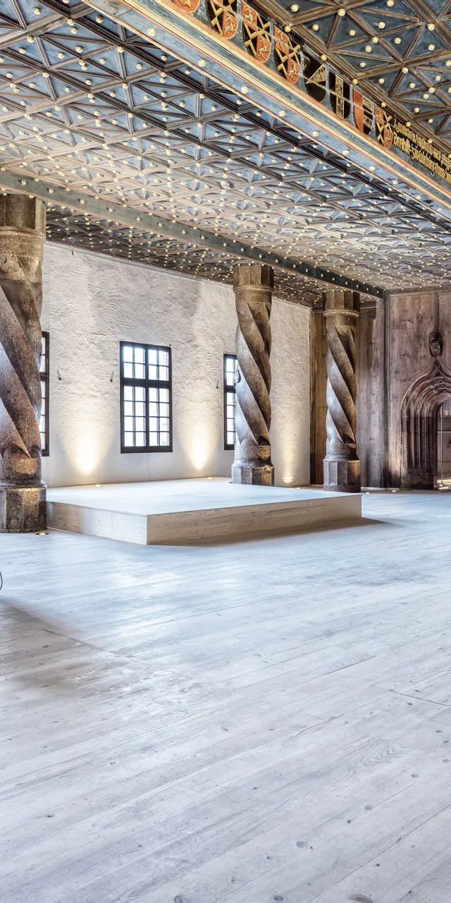 Historischer Saal mit verzierten Säulen, Holzboden und dekorierter Decke