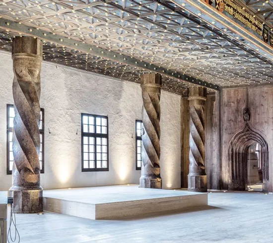Historischer Saal mit gedrehten Steinsäulen, Holzvertäfelung und kunstvoller Decke im Schlossinneren