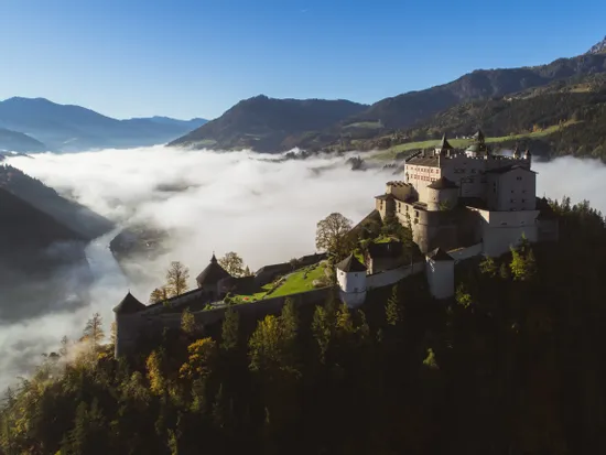 Mittelalterliche Burg auf einem Hügel mit Blick auf nebliges Tal und bewaldete Berge