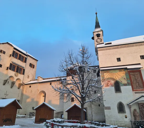 Verschneite Kirche und historische Gebäude mit Sonnenuhr und Holzständen im Winter