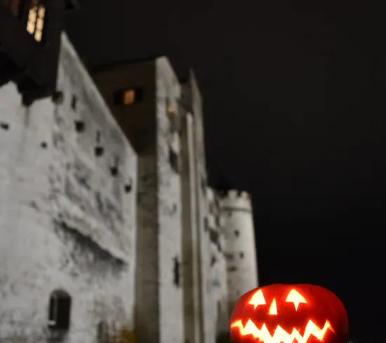 Leuchtender Kürbiskopf auf Steinmauer vor mittelalterlicher Burg bei Nacht