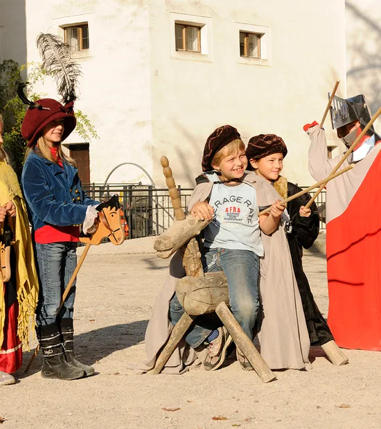 Bambini in costumi medievali giocano all'aperto con cavallucci a bastone e spade di legno