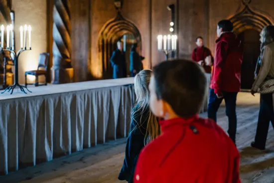 Besucher betrachten einen Saal im mittelalterlichen Stil mit Kerzenhaltern und Holzverzierungen