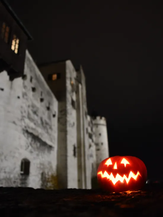 Leuchtender Kürbiskopf auf Steinmauer vor mittelalterlicher Burg bei Nacht