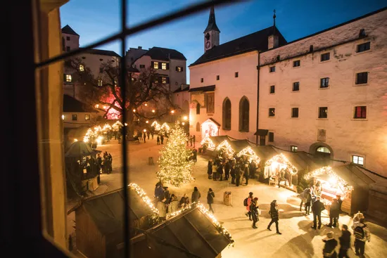 Crowd enjoying illuminated Christmas market in medieval courtyard at dusk