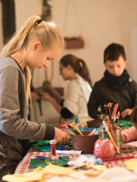 Children doing Christmas crafts at a table with colored paper, pencils, and decorations