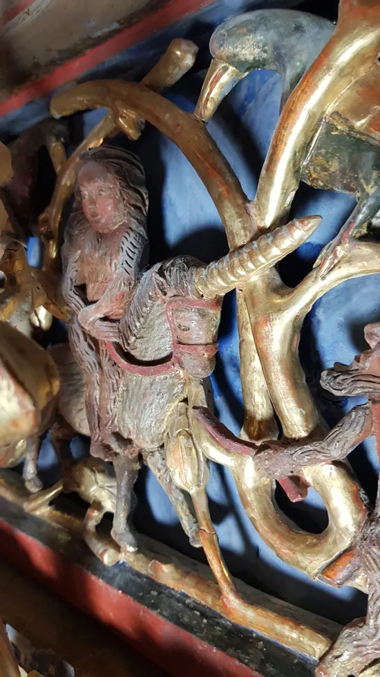 Medieval wood carving of a woman riding a unicorn surrounded by golden branches