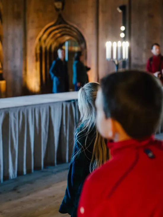 Visitors viewing a medieval-style hall with candle stands and wooden architecture