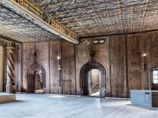 Historic hall with twisted stone columns, wooden walls, and ornate ceiling in castle interior
