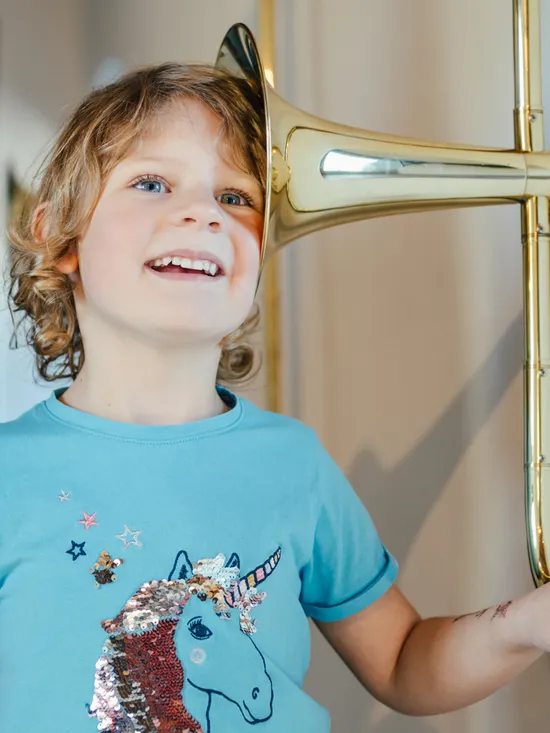 Lächelndes Kind mit Einhorn-Shirt hört durch antikes Messing-Sprachrohr