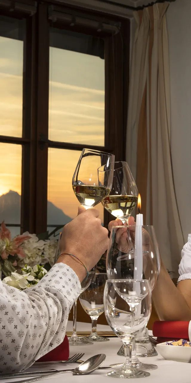 Paar stößt bei Sonnenuntergang in einem gemütlichen Restaurant mit Weingläsern an