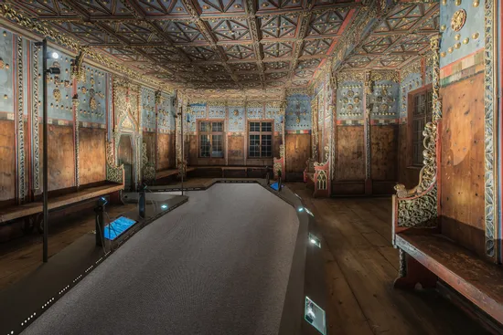 Ornate historic wooden hall with painted ceiling and carved benches in museum exhibit